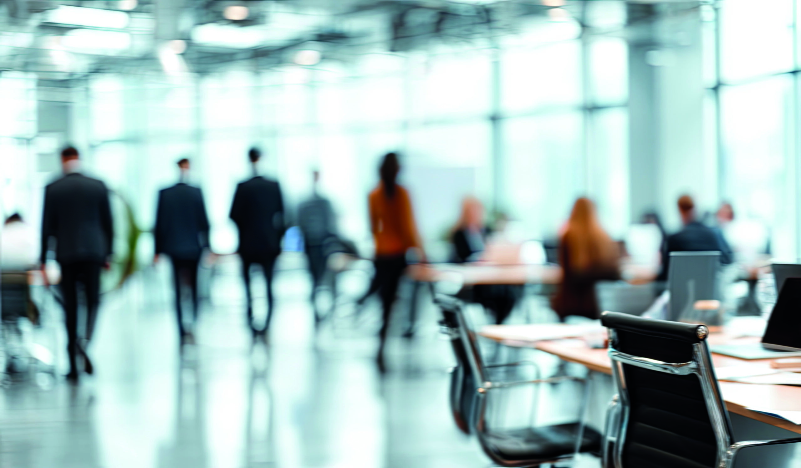 Blurry,View,Of,People,Walking,In,A,Modern,,Sunlit,Office